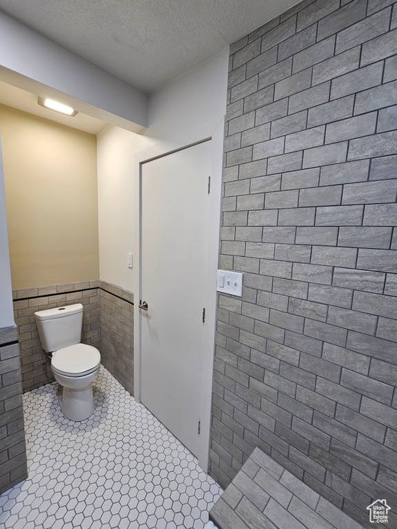 Bathroom with tile walls, tile patterned flooring, a textured ceiling, and toilet