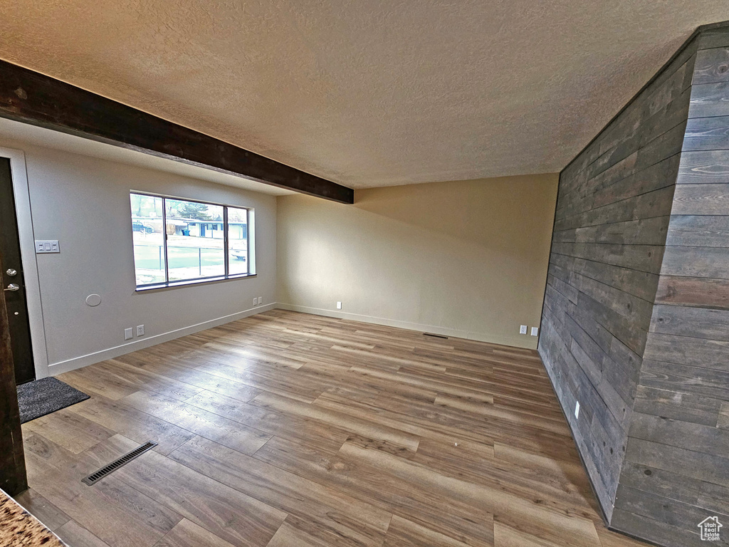 Unfurnished living room with a textured ceiling, light hardwood / wood-style floors, and beamed ceiling