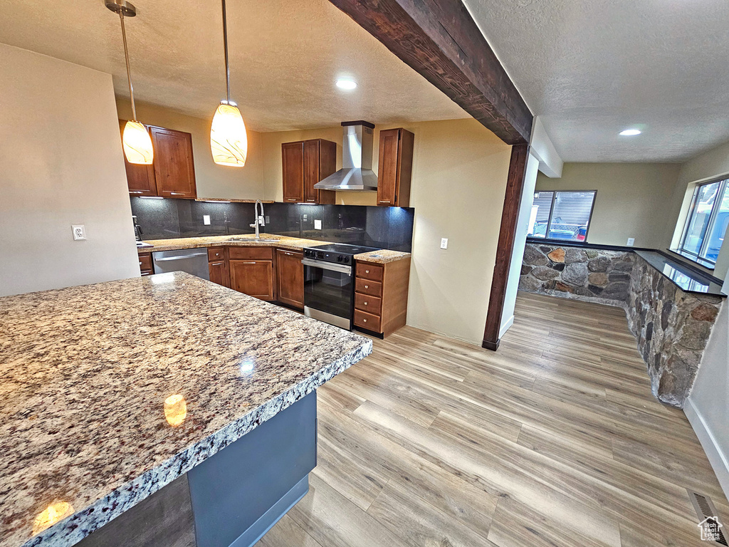 Kitchen featuring sink, decorative light fixtures, stainless steel appliances, decorative backsplash, and wall chimney range hood