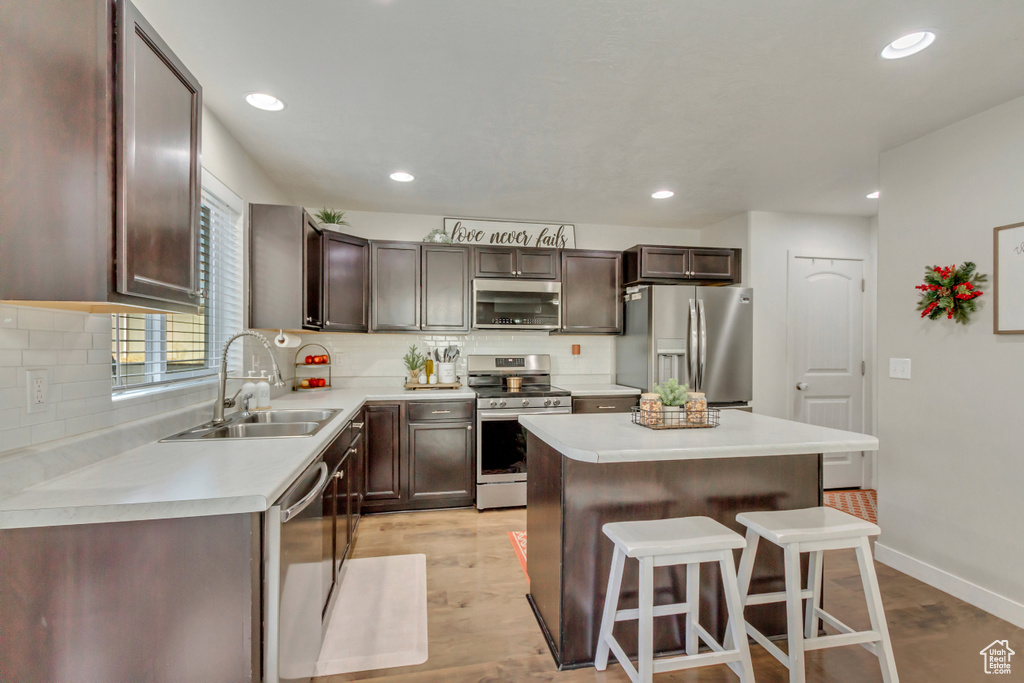 Kitchen with a kitchen breakfast bar, sink, light wood-type flooring, appliances with stainless steel finishes, and a kitchen island