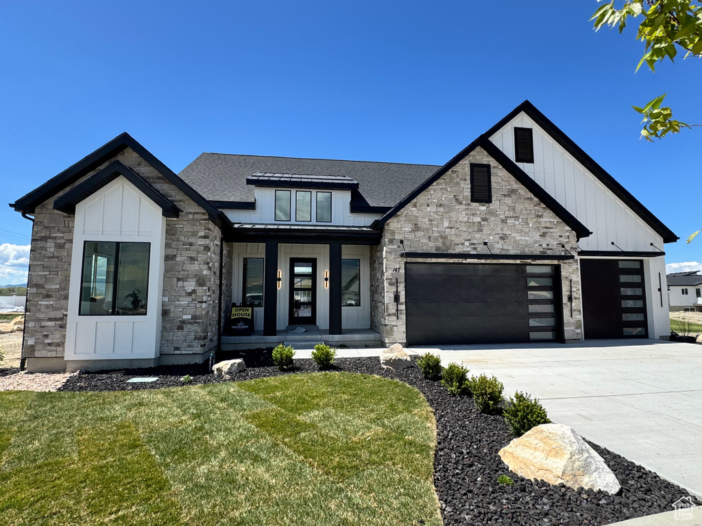 Modern inspired farmhouse featuring stone siding, a porch, an attached garage, a front yard, and board and batten siding