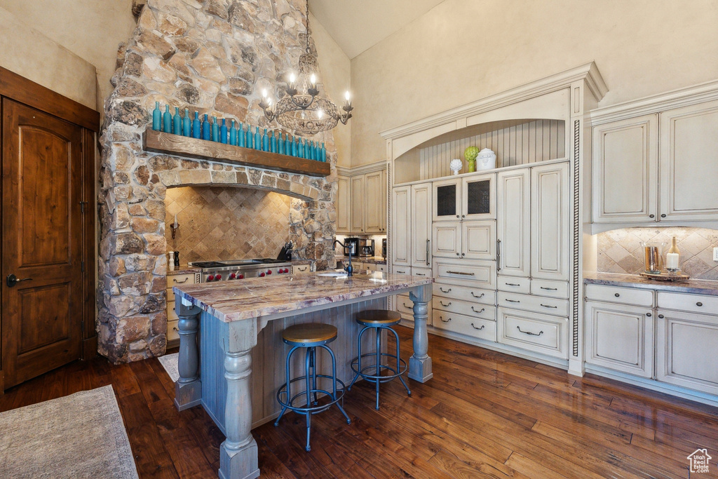 Kitchen with tasteful backsplash, cream cabinets, dark wood-style floors, a kitchen island with sink, and high vaulted ceiling