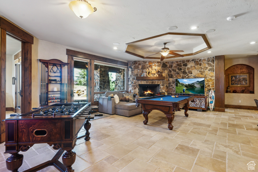 Recreation room featuring a ceiling fan, a raised ceiling, billiards table, a stone fireplace, and stone tile flooring