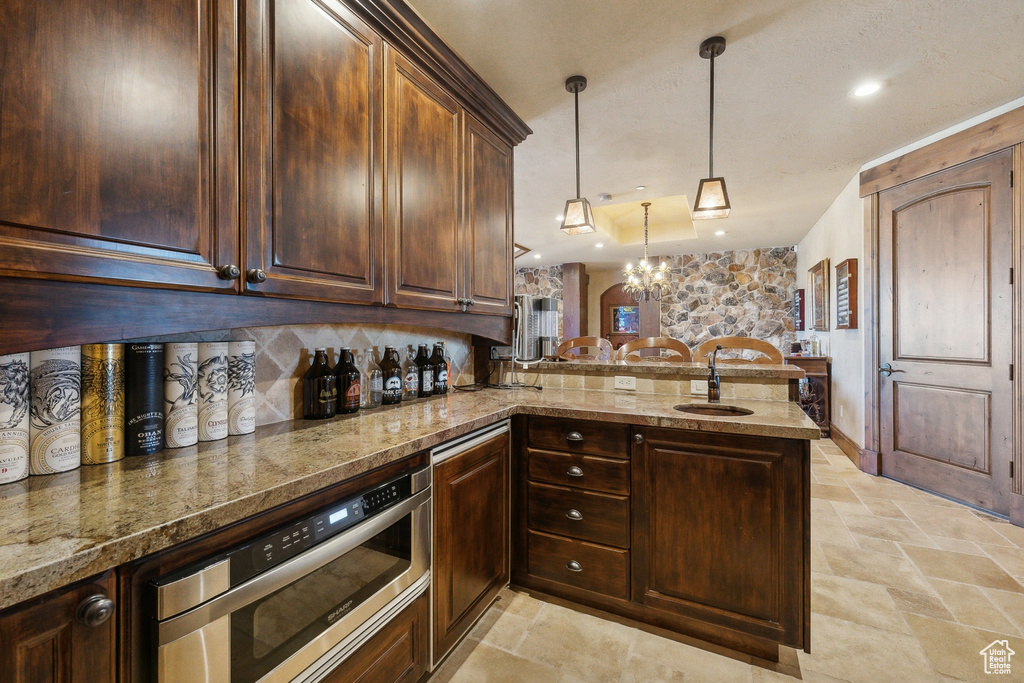 Kitchen with a sink, a peninsula, backsplash, light stone finish flooring, and stainless steel microwave