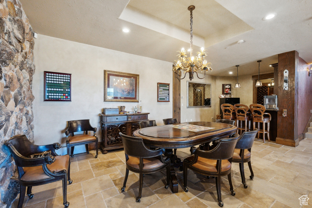 Dining area with stone tile flooring, a raised ceiling, a chandelier, and recessed lighting