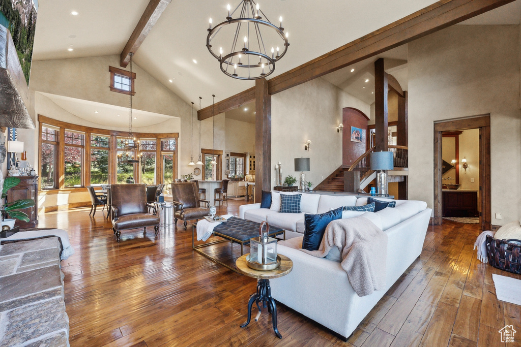 Living room featuring high vaulted ceiling, beamed ceiling, hardwood / wood-style flooring, a chandelier, and stairway
