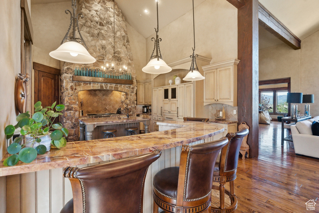 Kitchen with high vaulted ceiling, dark wood-style flooring, a breakfast bar, beamed ceiling, and cream cabinets