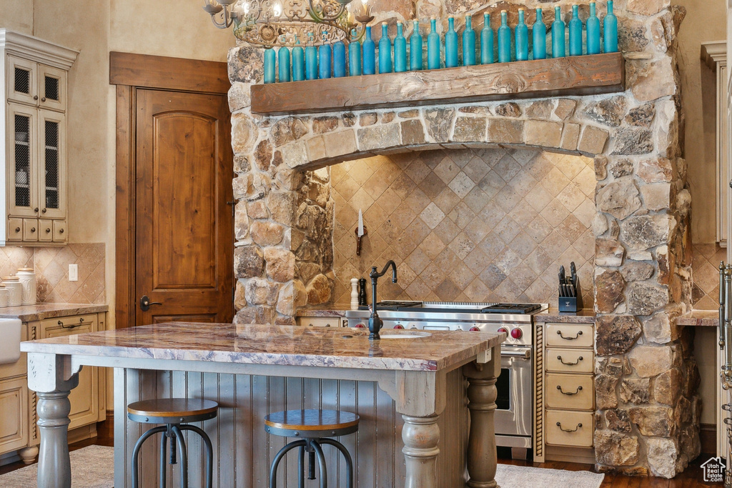 Kitchen featuring stainless steel range, tasteful backsplash, cream cabinetry, and a kitchen bar