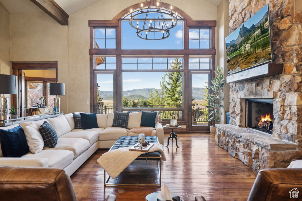 Living area with high vaulted ceiling, a chandelier, hardwood / wood-style floors, a stone fireplace, and beam ceiling