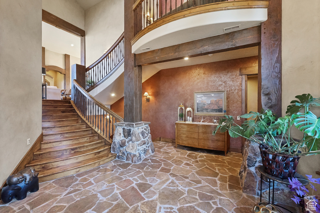 Foyer entrance featuring stone flooring, a towering ceiling, stairs, and baseboards