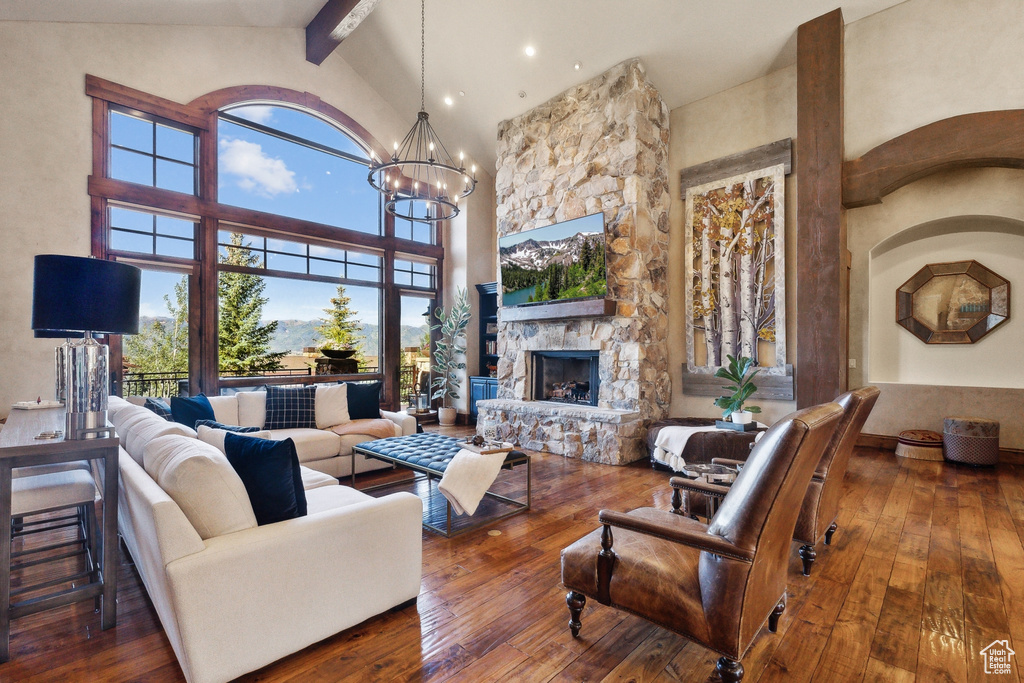 Living area with beam ceiling, high vaulted ceiling, wood-type flooring, a chandelier, and a fireplace