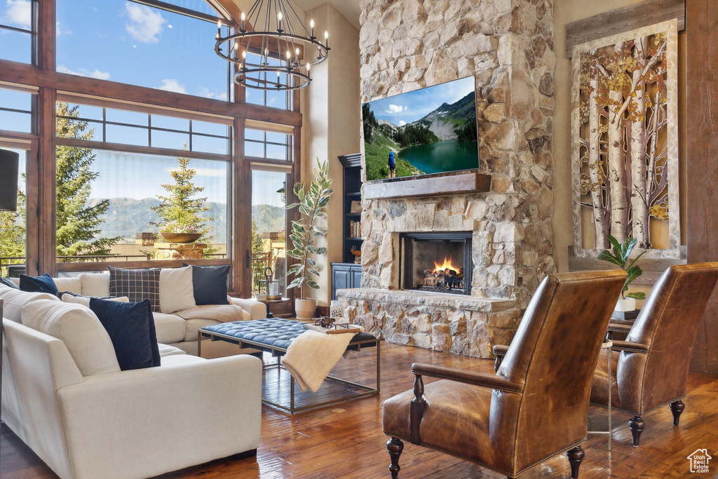 Living area with hardwood / wood-style floors, a chandelier, a stone fireplace, and a towering ceiling