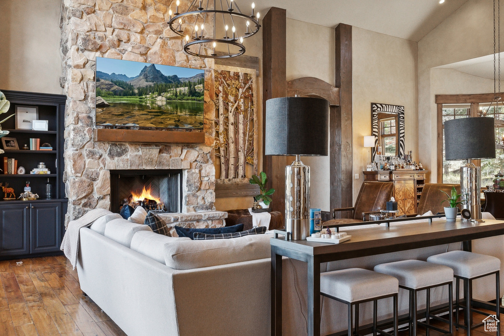 Living room featuring hardwood / wood-style floors, a chandelier, a stone fireplace, and high vaulted ceiling