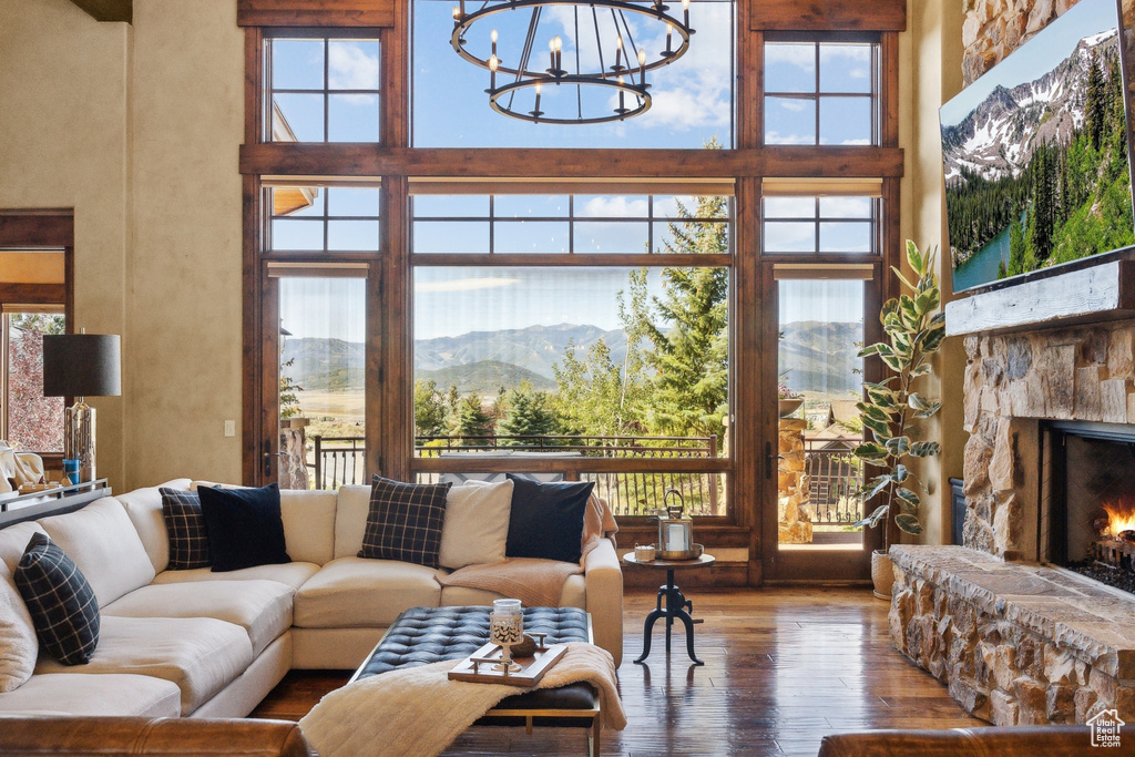 Living area featuring a high ceiling, wood-type flooring, a chandelier, and a stone fireplace