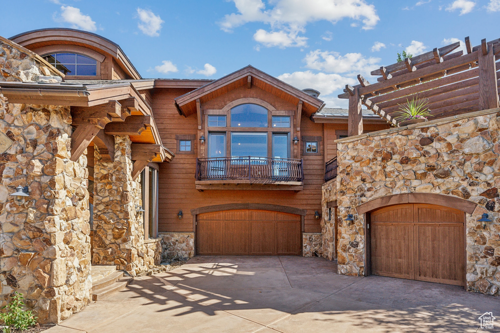 View of front of house featuring stone siding, a balcony, driveway, and a garage