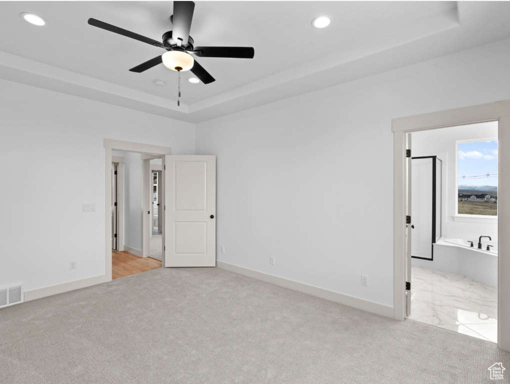 Unfurnished bedroom featuring light colored carpet, recessed lighting, a raised ceiling, baseboards, and ensuite bath