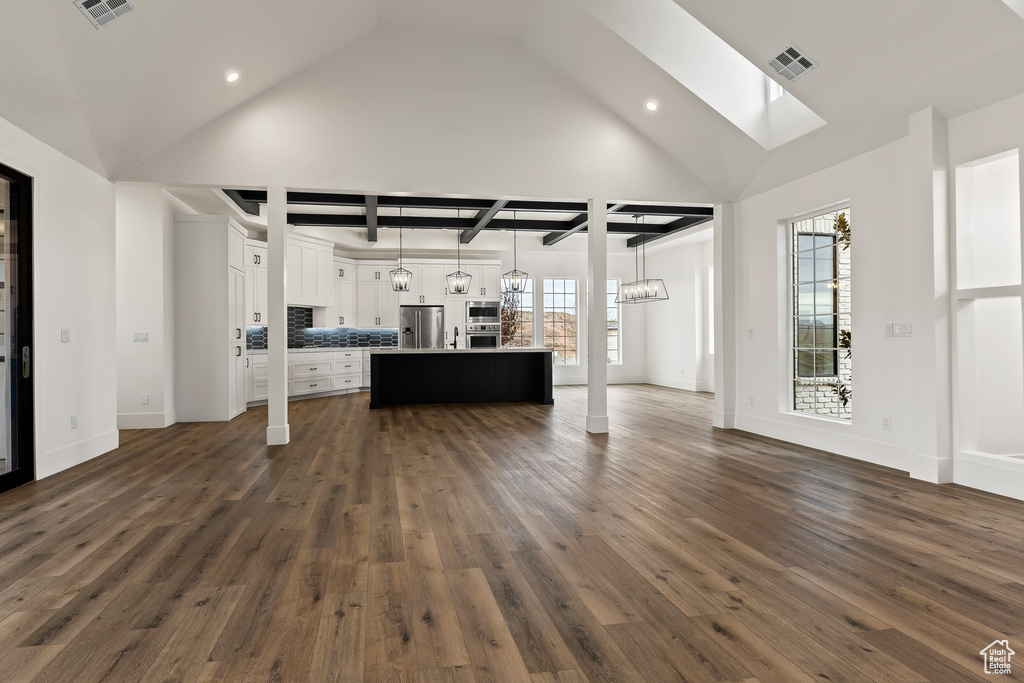 Unfurnished living room featuring dark hardwood / wood-style flooring, a skylight, high vaulted ceiling, and a chandelier