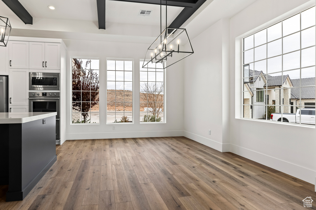 Unfurnished dining area featuring a chandelier, beam ceiling, and light hardwood / wood-style flooring