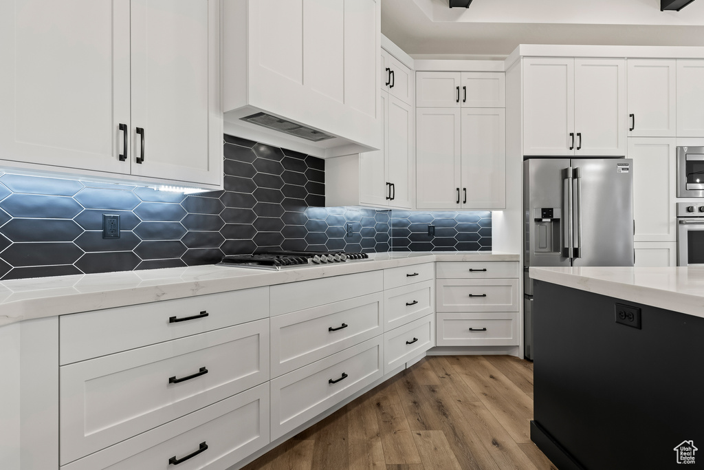 Kitchen with appliances with stainless steel finishes, tasteful backsplash, light stone counters, light hardwood / wood-style flooring, and white cabinetry