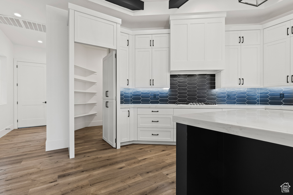 Kitchen with decorative backsplash, wood-type flooring, white cabinetry, and light stone counters