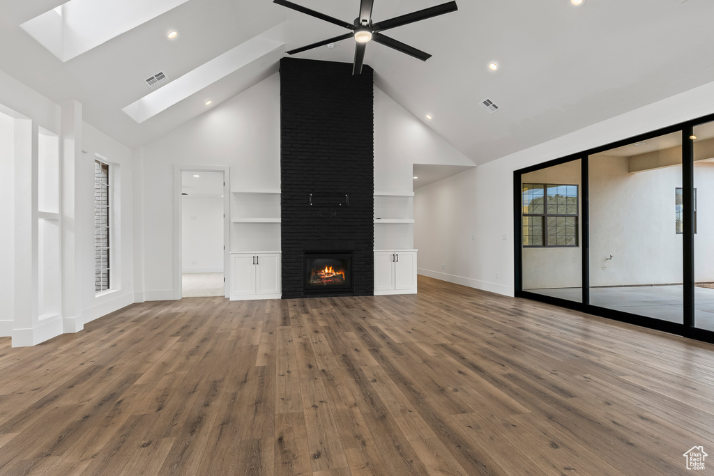 Unfurnished living room featuring a large fireplace, wood-type flooring, high vaulted ceiling, and a skylight