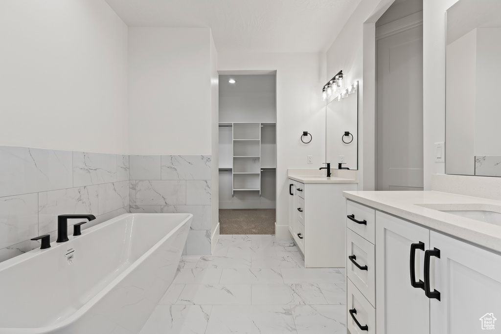 Bathroom featuring a tub to relax in, vanity, and tile walls