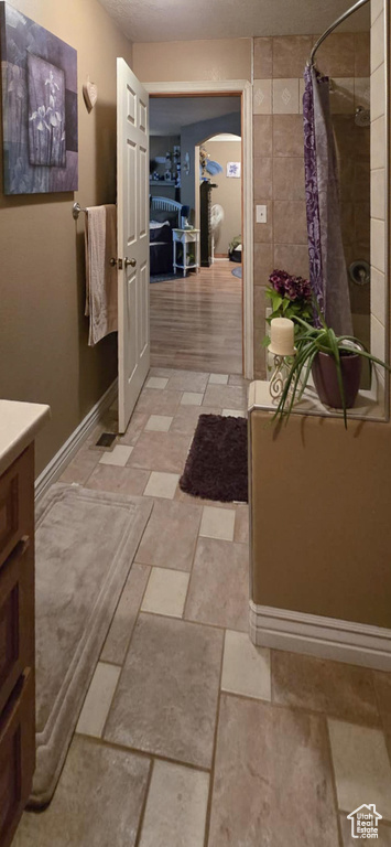 Full bathroom with a textured ceiling, baseboards, tiled shower, and vanity