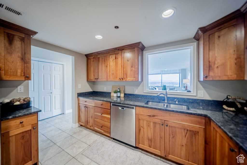 Kitchen with light tile patterned flooring, stainless steel dishwasher, dark stone counters, and sink