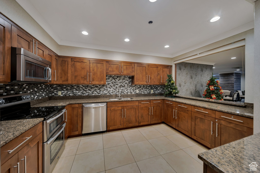Kitchen with appliances with stainless steel finishes, backsplash, sink, light tile patterned floors, and stone counters