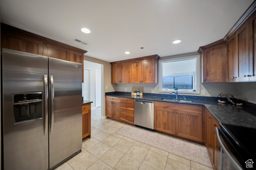 Kitchen featuring light tile patterned flooring, stainless steel appliances, dark stone countertops, and sink