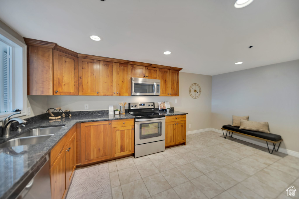 Kitchen with sink, light tile patterned floors, stainless steel appliances, and dark stone counters