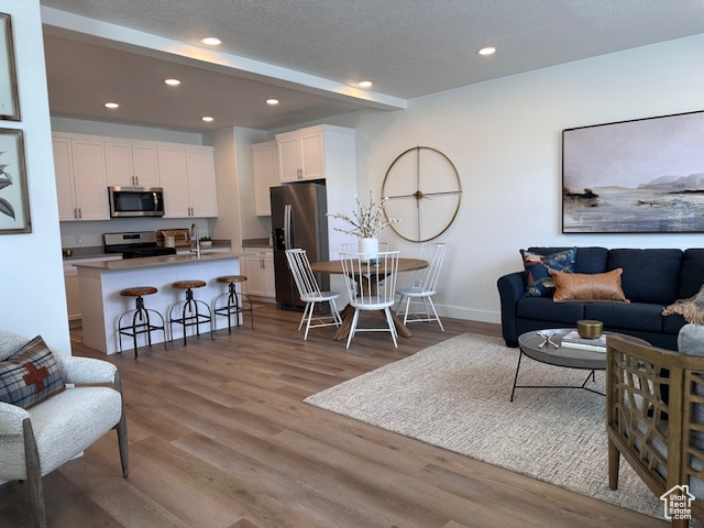 Living room featuring recessed lighting, light wood-type flooring, baseboards, and a textured ceiling