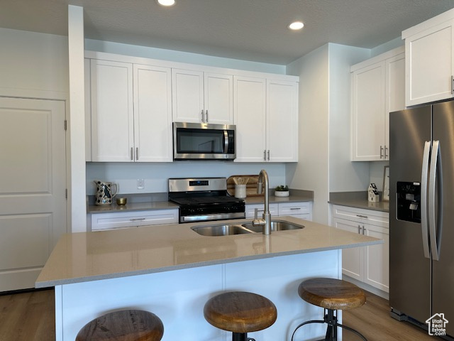 Kitchen with stainless steel appliances, a sink, wood finished floors, a breakfast bar area, and recessed lighting