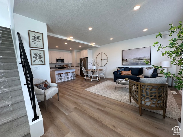 Living room featuring stairs, wood finished floors, a textured ceiling, recessed lighting, and baseboards