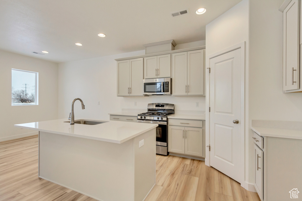 Kitchen featuring an island with sink, a sink, light wood-type flooring, stainless steel appliances, and visible vents