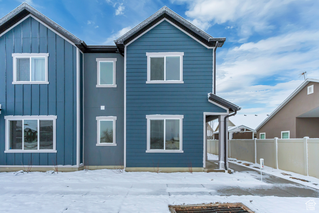 Snow covered rear of property featuring board and batten siding and fence