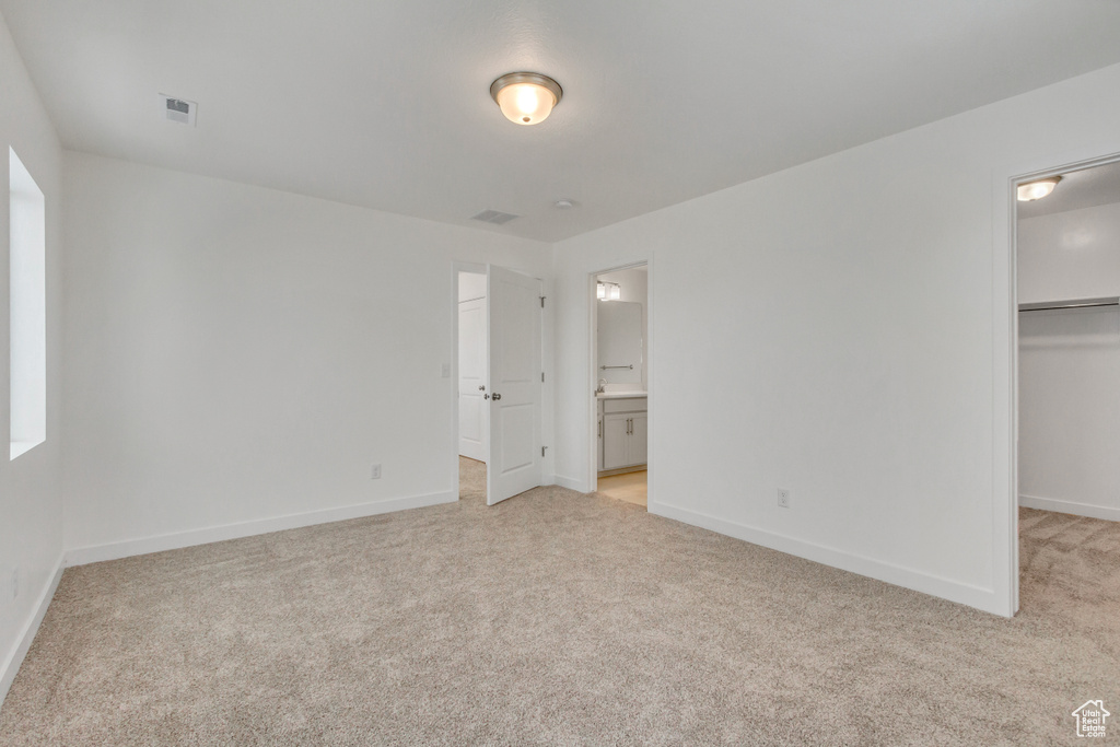 Unfurnished bedroom with a closet, baseboards, a walk in closet, and light carpet