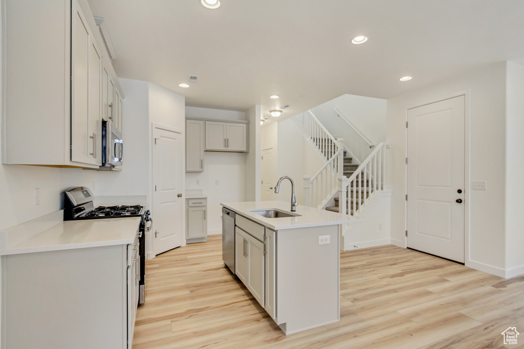 Kitchen featuring a sink, light wood finished floors, stainless steel appliances, a kitchen island with sink, and recessed lighting