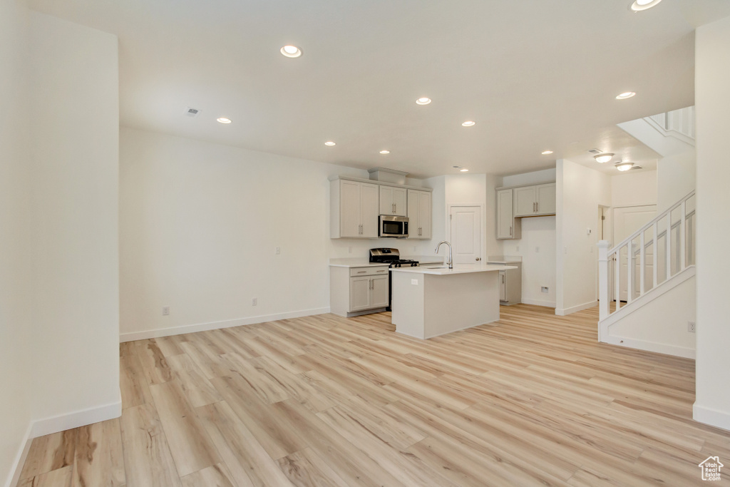 Kitchen with light wood-type flooring, a kitchen island with sink, stainless steel appliances, and recessed lighting