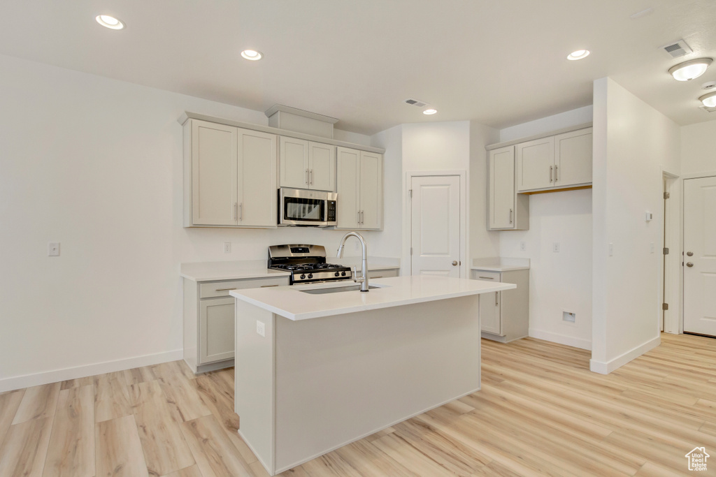Kitchen with baseboards, light wood-style flooring, an island with sink, and stainless steel appliances