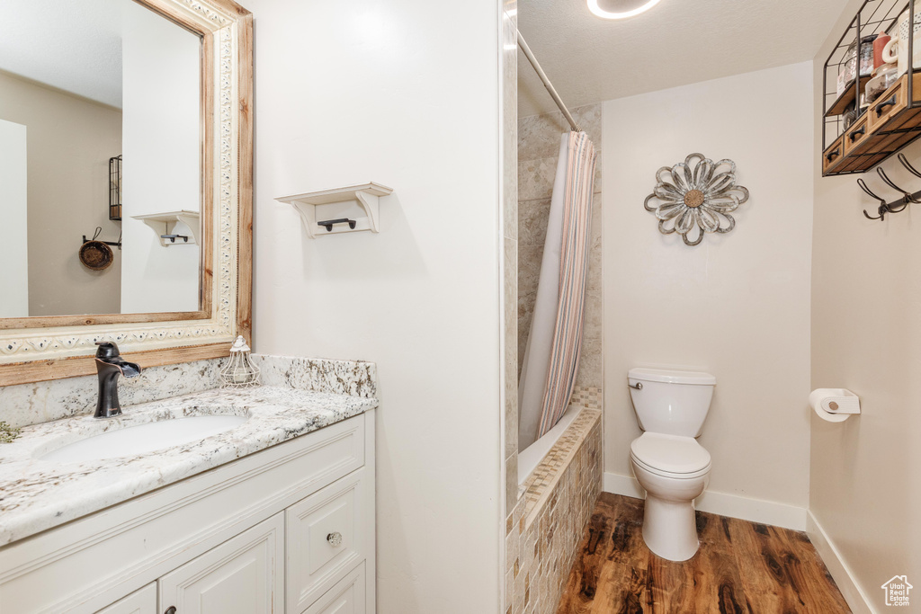 Bathroom with wood finished floors, shower / bath combination with curtain, toilet, vanity, and baseboards