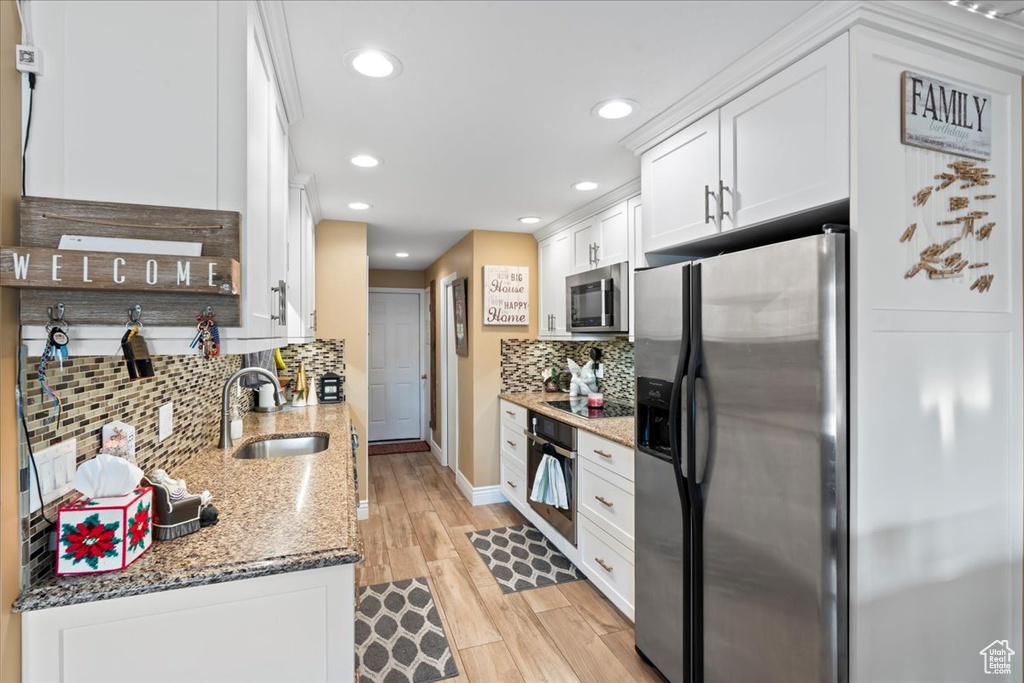 Kitchen featuring sink, decorative backsplash, dark stone countertops, appliances with stainless steel finishes, and white cabinetry