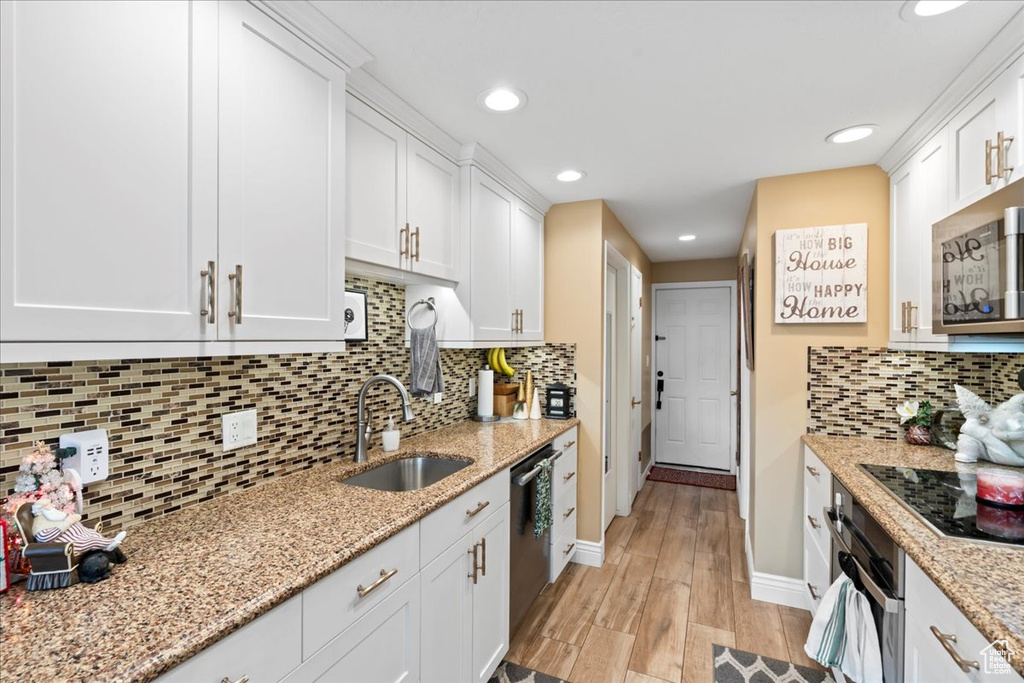 Kitchen with appliances with stainless steel finishes, light stone counters, sink, light hardwood / wood-style flooring, and white cabinetry