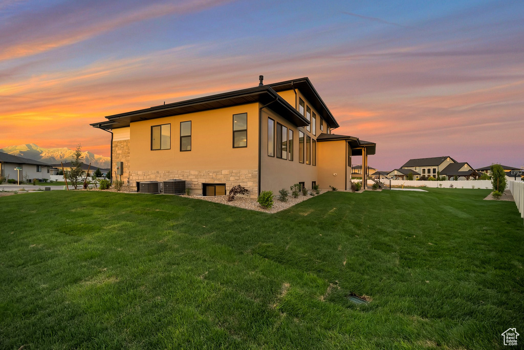Property exterior at dusk featuring a yard and central air condition unit