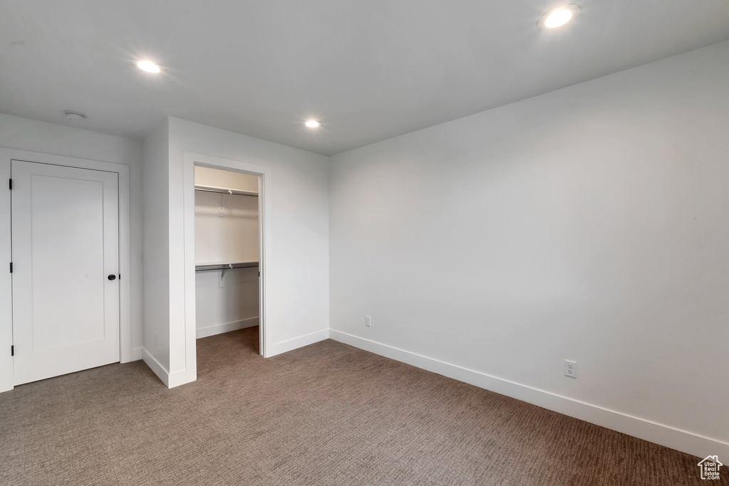 Unfurnished bedroom with dark colored carpet, a walk in closet, and a closet