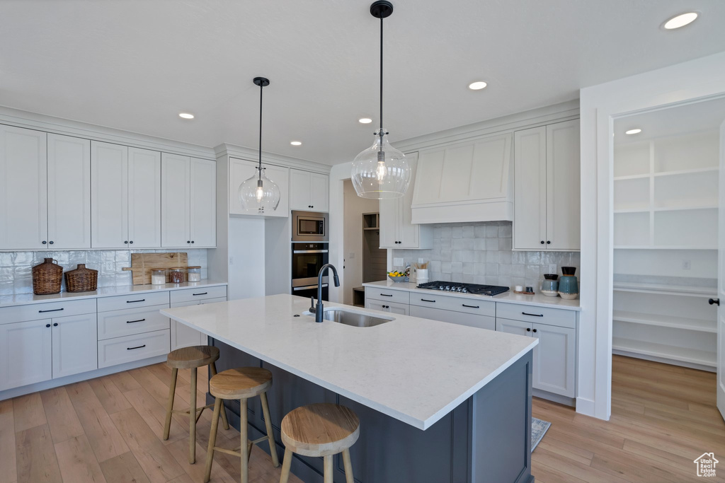 Kitchen featuring gas stovetop, sink, white cabinets, stainless steel microwave, and an island with sink