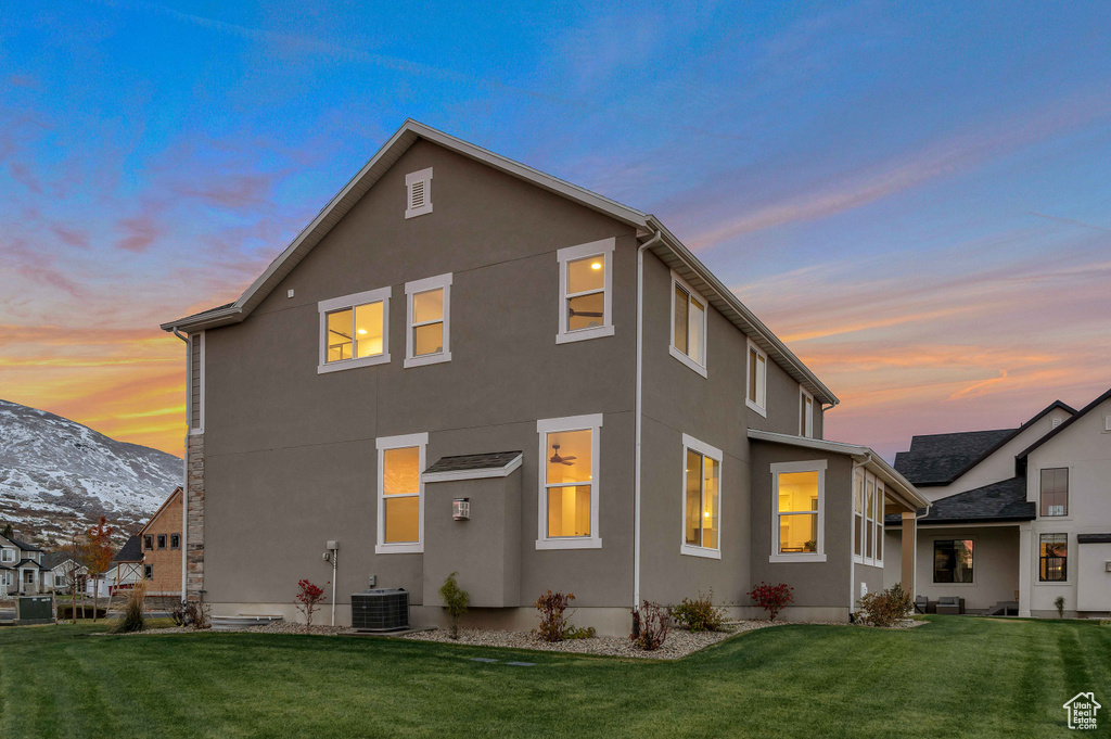 Back house at dusk featuring a yard and cooling unit