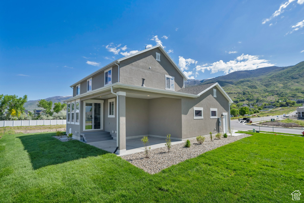 Rear view of property with a lawn, a mountain view, and a patio