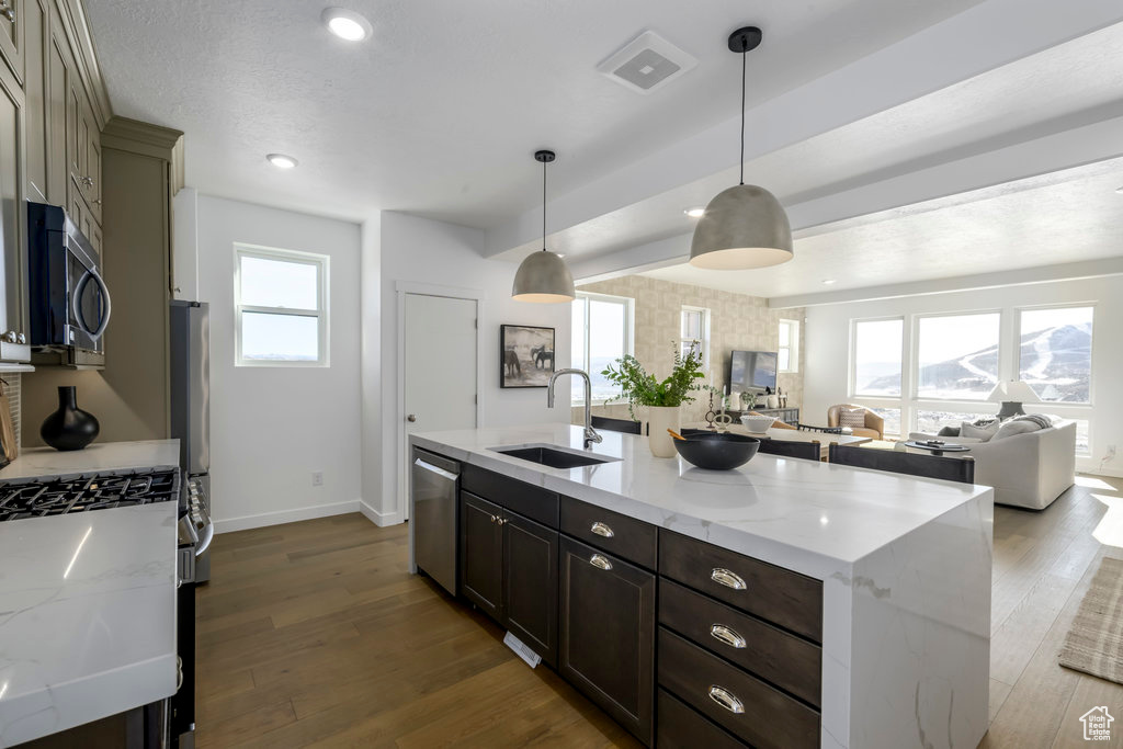 Kitchen featuring a sink, baseboards, light stone counters, open floor plan, and stainless steel appliances