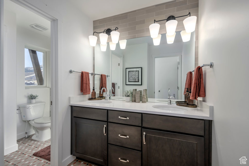 Bathroom featuring double vanity, a sink, baseboards, and toilet
